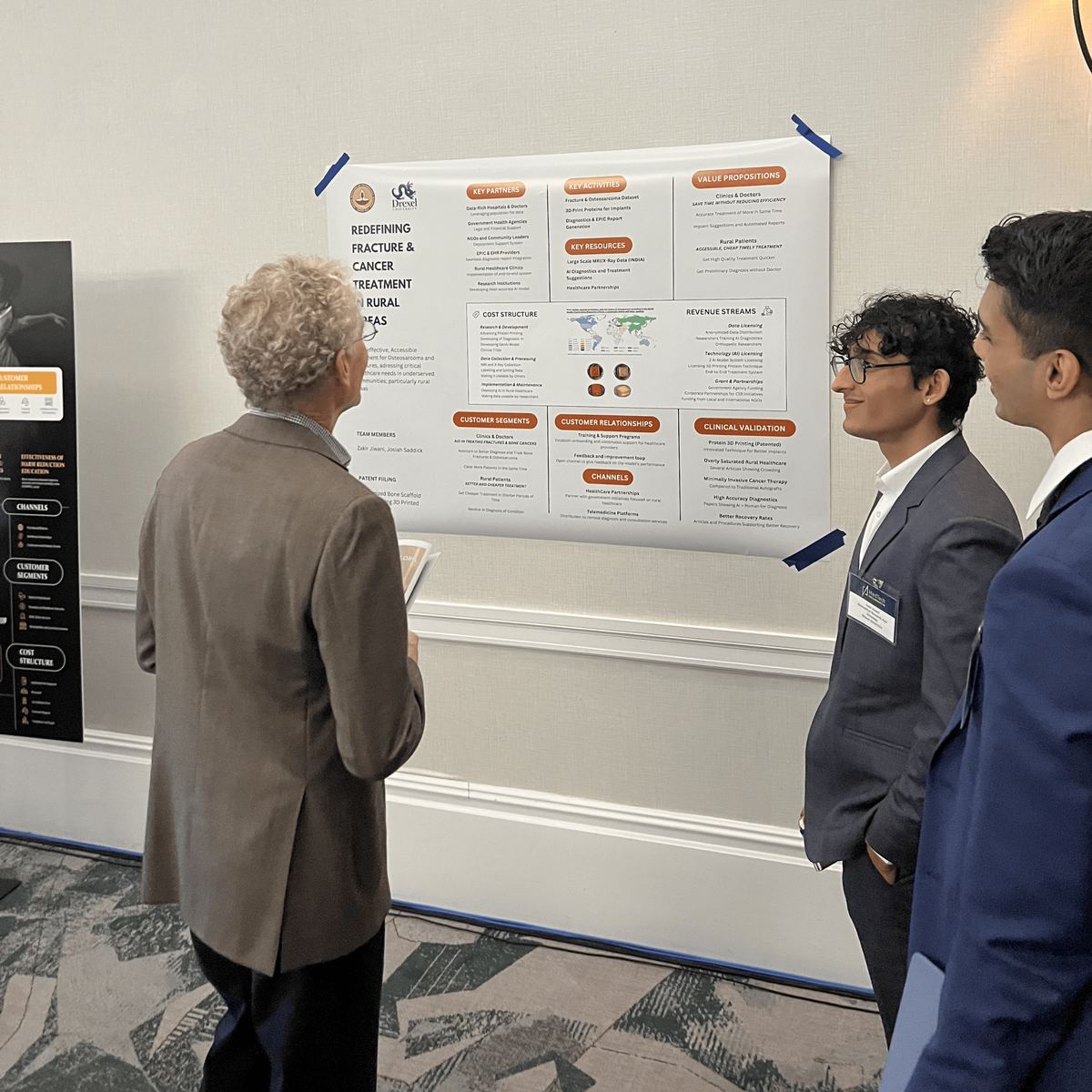 Two students presenting their Business Model Canvas poster to an attendee at the Innovation Showcase