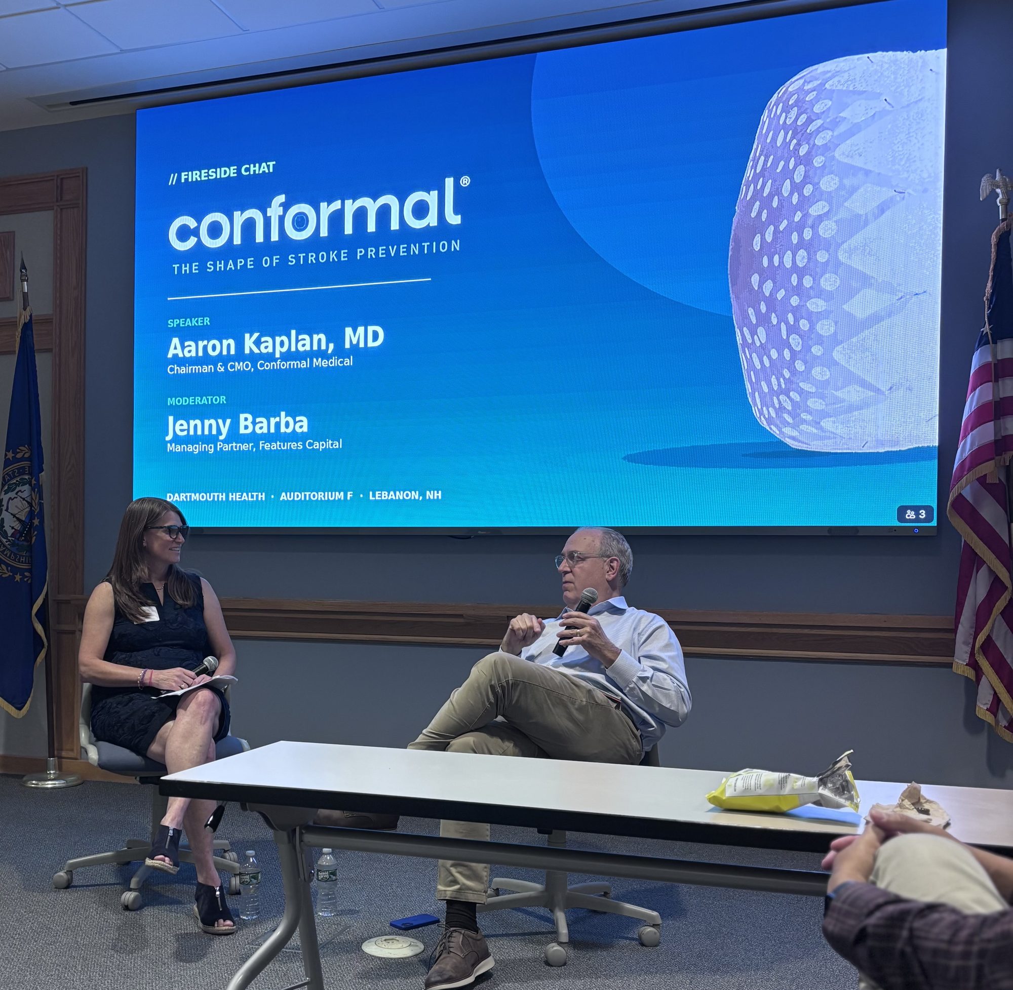 Jenny Barba interviews Aaron Kaplan, MD on stage at Dartmouth Health, seated in front of a Conformal Medical fireside chat title slide.